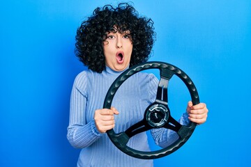 Young middle east woman holding steering wheel afraid and shocked with surprise and amazed expression, fear and excited face.