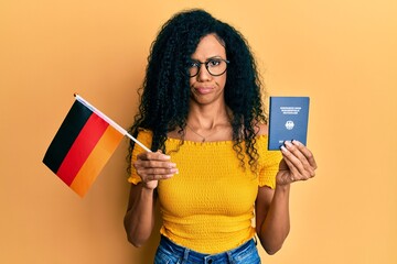 Middle age african american woman holding germany flag and passport skeptic and nervous, frowning...
