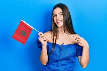 Zelfklevend Fotobehang Young brunette teenager holding morocco flag smiling happy pointing with hand and finger © Krakenimages.com