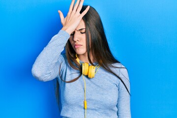 Young brunette teenager wearing headphones on neck surprised with hand on head for mistake,...