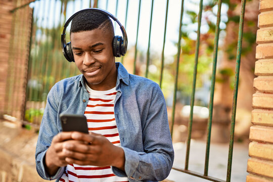 Young african american man using smartphone and headphones at the city.