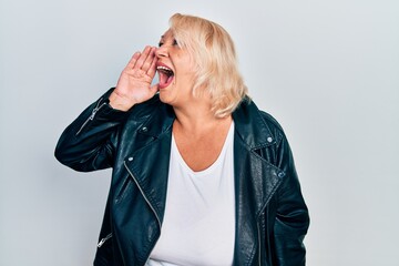 Middle age blonde woman wearing leather jacket shouting and screaming loud to side with hand on mouth. communication concept.