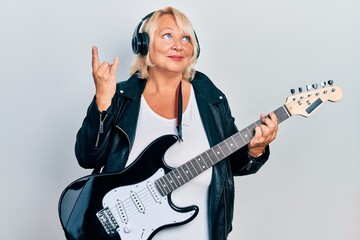 Middle age blonde woman playing electric guitar doing horns sign with fingers smiling looking to...