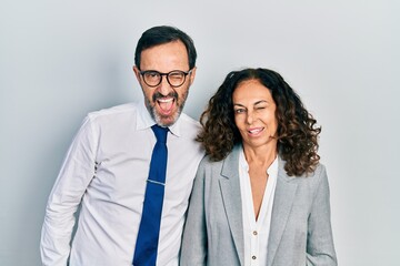 Middle age couple of hispanic woman and man wearing business office uniform winking looking at the camera with sexy expression, cheerful and happy face.