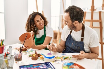 Two middle age students smiling happy painting clay sculpture at art school.