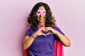Middle age hispanic woman wearing super hero costume smiling in love doing heart symbol shape with...
