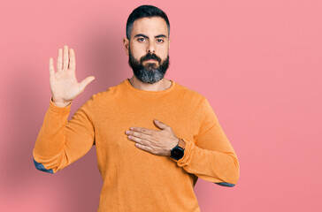 Hispanic man with beard wearing casual winter sweater swearing with hand on chest and open palm,...