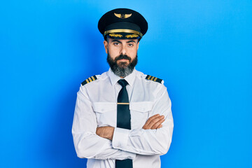 Young hispanic man wearing airplane pilot uniform with arms crossed gesture relaxed with serious expression on face. simple and natural looking at the camera.