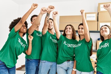 Obraz premium Group of young volunteers smiing happy with fists raised up at charity center.