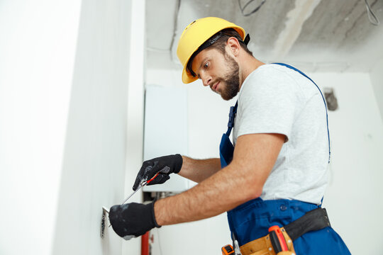 Male Worker Professional Electrician In Uniform Installing Electrical Outlet In Apartment After Renovation Work