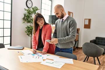 Two hispanic business workers with serious expression working using smartphone at the office.