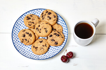 White cup with coffee, traditional cookies and sweet cherries on a white wooden background, closeup. Tasty breakfast, morning routine concept