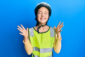 Beautiful brunette little girl wearing bike helmet and reflective vest celebrating mad and crazy for success with arms raised and closed eyes screaming excited. winner concept