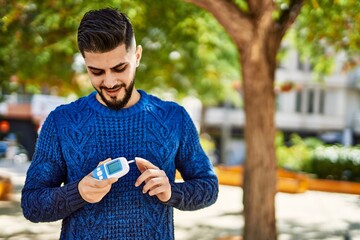 Young arab man smiling confident holding glucometer at park