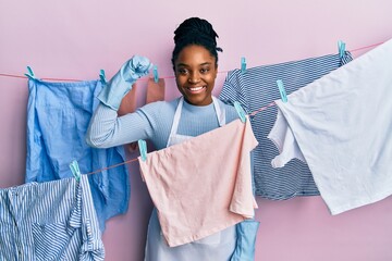 African american woman with braided hair washing clothes at clothesline strong person showing arm muscle, confident and proud of power