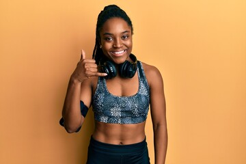 African american woman with braided hair wearing sportswear and arm band smiling doing phone gesture with hand and fingers like talking on the telephone. communicating concepts.