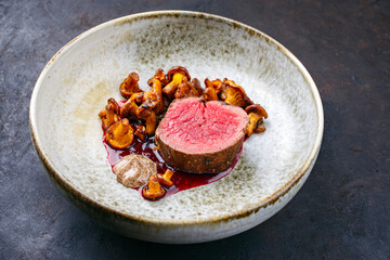 Modern Style traditionelles fried dry aged Angus Rinderfilet mit Pfifferling Mousse Parfait und Wildkirsch Relish Creme serviert als close-up auf einem Nordic Design Teller 