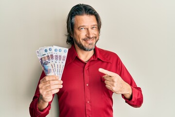 Middle age handsome man holding russian 500 ruble banknotes smiling happy pointing with hand and...
