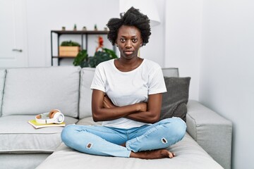 African young woman sitting on the sofa at home skeptic and nervous, disapproving expression on face with crossed arms. negative person.