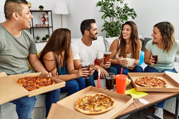 Group of young hispanic friends smiling happy eating italian pizza sitting on the sofa at home.