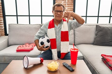 Senior man watching football holding ball supporting team with angry face, negative sign showing...