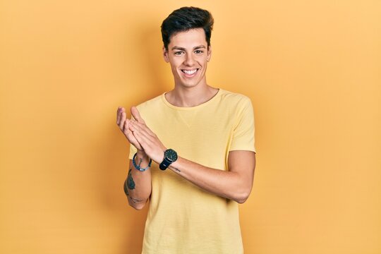 Young hispanic man wearing casual yellow t shirt clapping and applauding happy and joyful, smiling proud hands together