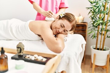Obraz na płótnie Canvas Middle age caucasian woman having back massage using thai hot bags at beauty center