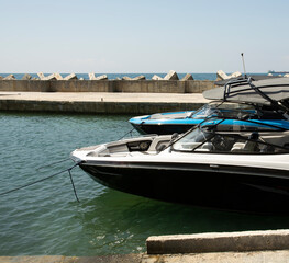 two high-speed boats moored to the pier against the background of the sea and a concrete breakwater