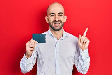 Young bald man holding ssd memory smiling happy pointing with hand and finger to the side
