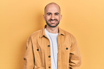 Young bald man wearing casual clothes looking positive and happy standing and smiling with a confident smile showing teeth