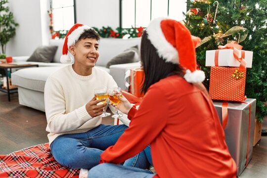Young hispanic couple smiling happy wearing christmas hat toasting with champagne at home.