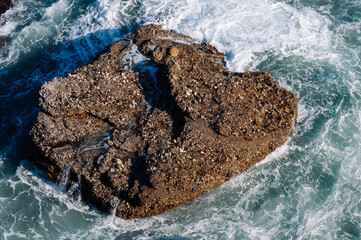 Aerial drone view of the ocean and waves crashing on rocks.