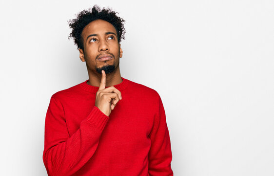 Young african american man with beard wearing casual winter sweater thinking concentrated about doubt with finger on chin and looking up wondering