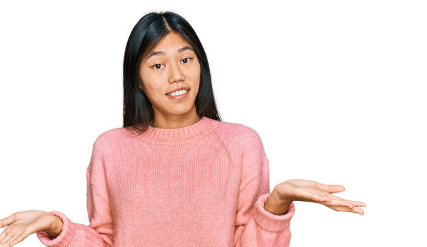 Beautiful young asian woman wearing casual winter sweater clueless and confused expression with arms and hands raised. doubt concept.