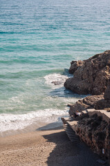 Aerial top view of sea waves hitting rocks on the beach with turquoise sea water. 