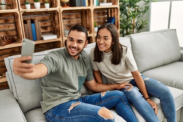 Young latin couple smiling happy making selfie by the smartphone at home.