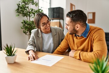Couple smiling happy reading document at the office.