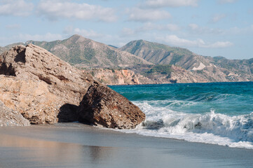 Aerial top view of sea waves hitting rocks on the beach with turquoise sea water. 