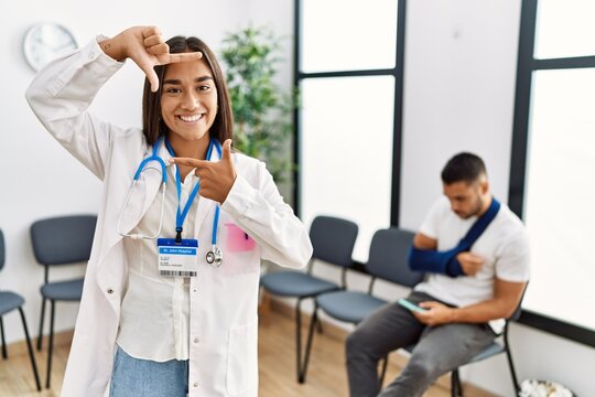 Young asian doctor woman at waiting room with a man with a broken arm smiling making frame with hands and fingers with happy face. creativity and photography concept.