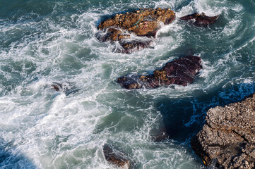 Aerial drone view of the ocean and waves crashing on rocks.