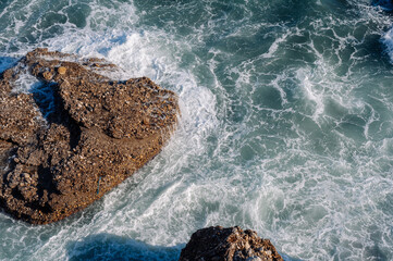 Aerial drone view of the ocean and waves crashing on rocks.