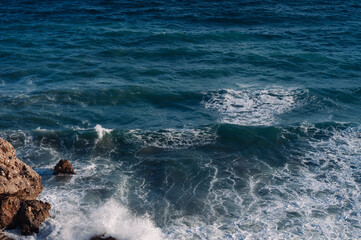 Aerial drone view of the ocean and waves crashing on rocks.