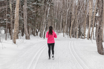 Winter Running in Snow. Woman runner training outside on cold winter day in forest. Fit healthy lifestyle photo with young fitness model. Girl running away in full length in winter running shoes