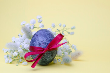 Easter blue egg with gypsophila flowers on a yellow background. Festive postcard for congratulations. Natural dye karkade tea.