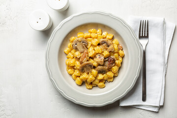 Potato gnocchi with champs, porcini mushrooms and melted butter. Top view, white table surface.