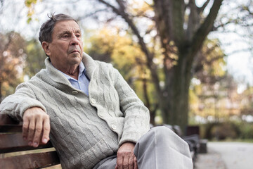 Portrait of a pensive senior man sitting on the bench, in the public park, outdoors. Old man...