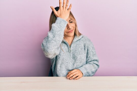 Young caucasian woman wearing casual clothes sitting on the table surprised with hand on head for mistake, remember error. forgot, bad memory concept.
