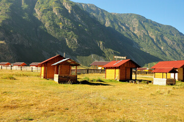 Several guest houses with a fence stand in a picturesque valley surrounded by high mountains.