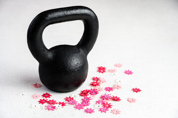 Fototapeta na wymiar Kettlebell spring fitness, black kettlebell on a white background with silver sparkles and red, pink, and white flowers 