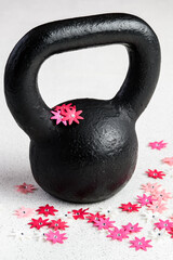 Fototapeta na wymiar Kettlebell spring fitness, black kettlebell on a white background with silver sparkles and red, pink, and white flowers 